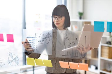 Modern teknoloji kavramı ve meşgul insanlar. Resmi giyinmiş, gözlüklü, kendine güveni tam beyaz bir kadın şirket yönetim kurulunda dikilirken dizüstü bilgisayarla iş sorunları çözüyordu..