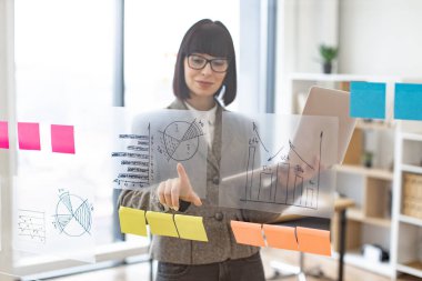 Modern teknoloji kavramı ve meşgul insanlar. Resmi giyinmiş, gözlüklü, kendine güveni tam beyaz bir kadın şirket yönetim kurulunda dikilirken dizüstü bilgisayarla iş sorunları çözüyordu..