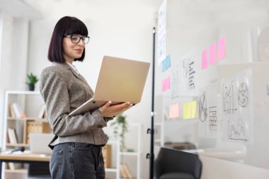 Modern teknoloji kavramı ve meşgul insanlar. Resmi giyinmiş, gözlüklü, kendine güveni tam beyaz bir kadın şirket yönetim kurulunda dikilirken dizüstü bilgisayarla iş sorunları çözüyordu..