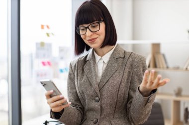 Gözlüklü zevkli iş kadını başarılı bir müzakere deneyimi yaşıyor. İş dünyasındaki beyaz kadın portresi. Resmi kıyafet kayıt videosu. Masada otururken cep telefonuyla kaydedilmiş..