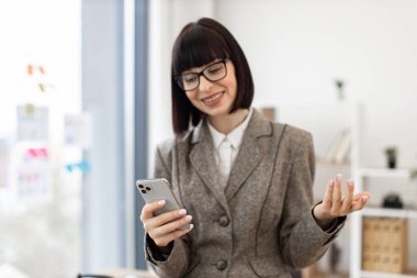 Personel toplantısında çevrimiçi sunum sırasında düşünceli bir Kafkas profesyonel konuşması. Ofis masasının yanında duran takım elbiseli, gülümseyen güzel bir kadın..