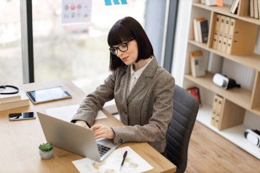 Teknolojiler üzerinden internet üzerinden bilgi arayan profesyonel girişimci, kopyalama alanı. Gözlüklü ve resmi giysili beyaz kadın ofis masasında otururken dizüstü bilgisayarla çalışıyor..