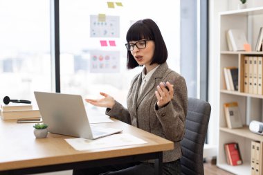 Planlanan online iş toplantısı sırasında neşeli beyaz iş arkadaşlarını selamlıyor. Resmi olarak gülümseyen iş kadını ofis masasında otururken bilgisayardan video mesajı alıyor..