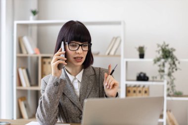 Deneyimli bir çalışan, iş yerindeki şirket verimliliğini arttırma fikrini ortaya attı. Resmi giyinen neşeli bayan dijital ekrandan rapor okurken akıllı telefondan konuşuyor..