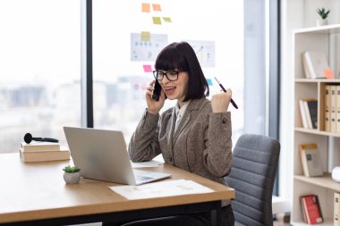 Verimli bir yönetici iş görüşmesi sırasında müşteriyle bilgi paylaşıyor. Ofisteki dizüstü bilgisayara bakarken cep telefonuyla konuşan gözlüklü çekici beyaz kadın..