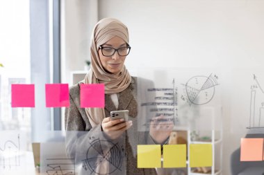 Resmi giyinmiş, tesettürlü, kendine güveni tam bir müslüman kadın. Şirket yönetim kurulunda telefon başında yazı yazarken iş sorunları çözüyormuş. Modern teknoloji ve meşgul insanlar kavramı.