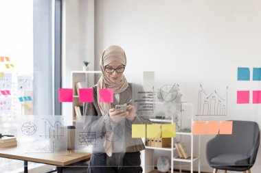 Resmi giyinmiş, tesettürlü, kendine güveni tam bir müslüman kadın. Şirket yönetim kurulunda telefon başında yazı yazarken iş sorunları çözüyormuş. Modern teknoloji ve meşgul insanlar kavramı.