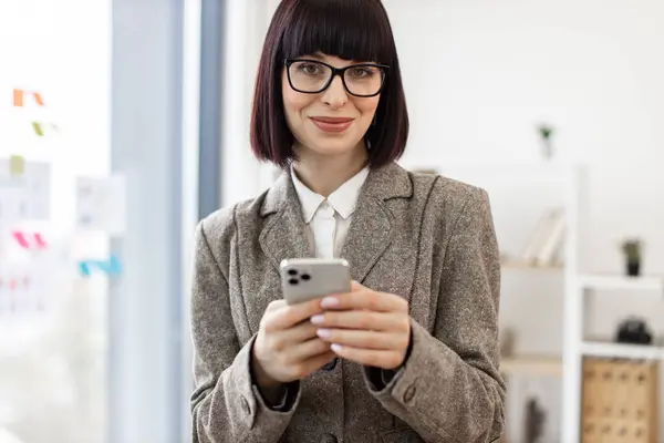 Smiling manager in suit developing electronic communication using wireless connection. Joyful caucasian business person in glasses replying to digital correspondence via cell phone at work, copy space