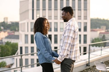 Aşk ilişkileri ve açık hava aktiviteleri kavramı. Genç Afrikalı çift, kadın ve erkek modern binanın çatısında sarılıyor ve birbirlerini arıyorlar..