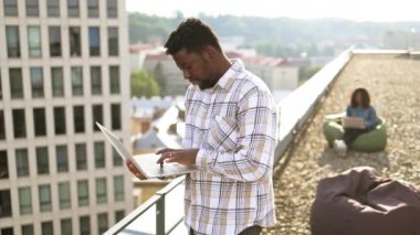 Bayan meslektaşım arka planda şezlongda otururken erkek güler yüzlü bir şekilde dışarıda dizüstü bilgisayar kullanıyor. Modern yaşam tarzı, bağlantı, iletişim, web sohbeti, sosyal medya, video konferans konsepti.