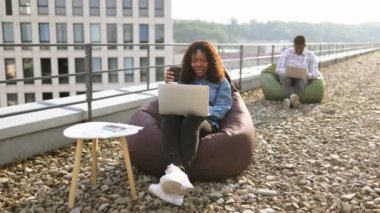 Kahve molası sırasında çatıda laptopa bakıp çığlık atan ve elini kaldıran Afrikalı Amerikalı bir kadın. Meslektaşı ise bulanık arka planda çalışıyor..