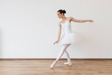Beyaz tulumlu beyaz balerin ve etekli balerin, bale unsurlarını sivri uçlu ayakkabılarla göstererek hareket ediyor. Stüdyo arka planında poz veren güzel genç bayan dansçı..