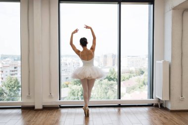 Beyaz tütü kostümlü, odaklanmış, beyaz bir beyaz balerin. Güzel bayan bale dansçısı büyük panoramik pencere önünde bale stüdyosunda piruet yapıyor..
