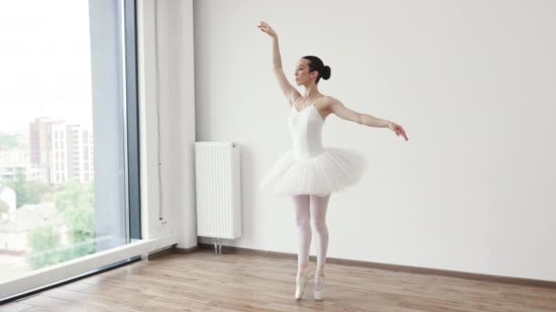 芭蕾课训练 高调轻柔调音 经典芭蕾舞者侧观 美丽优雅的芭蕾舞演员在白色灯堂靠近大窗户的白色短裙上练习芭蕾舞姿势 — 图库视频影像