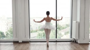 Beyaz salonda geniş pencerenin yanında beyaz etekli güzel balerin pozisyonları. Genç balerin - Bale stüdyosunda etekli uyumlu güzel kadın - Çağdaş dans sanatçısı.