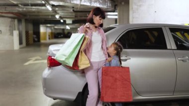 Çekici bir kadın aile, günlük giysiler içinde, neşeli bir beraberlik anını paylaşıyorlar. Yeraltı otoparkı, beyaz bir anne ve alışveriş merkezinden alınmış çantalı küçük bir kız..
