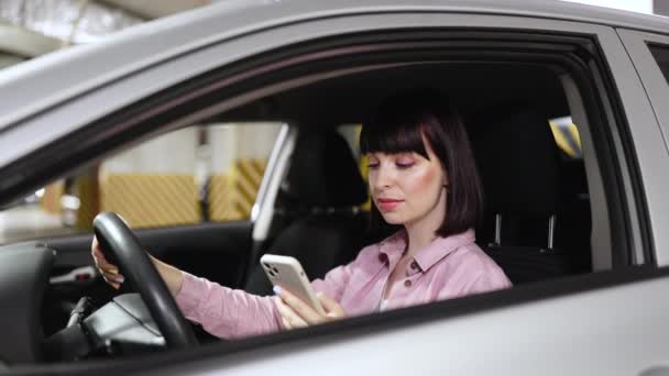 年轻自信的白种人女人穿着休闲装 坐在现代汽车的车轮后面 打电话 在地下停车场 — 图库视频影像