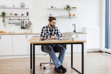 Dairede taşınabilir bilgisayar kullanarak şirket sorunlarını tartışan Kafkasyalı olumlu girişimci. Günlük giysiler içinde gülümseyen genç adam ofis çalışanlarıyla çevrimiçi konferans düzenliyor..