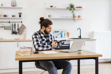Kablosuz kulaklığı olan, kendinden emin yetişkin biri evden online sunum yaparken grafik materyallere işaret ediyor. Modern teknolojileri kullanarak istatistiksel analiz sağlayan odaklı Kafkas işçisi