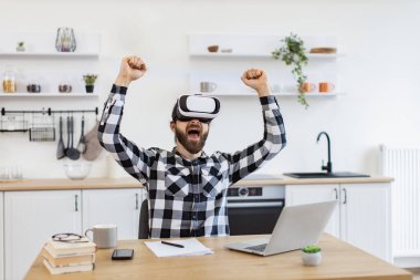 Neşeli sakallı adam VR kulaklık takıyor ve mutfakta çalışırken mutluluktan el kol hareketi yapıyor. Kafkas Teknoloji Yöneticisi yeni modern aygıtlardan memnun.