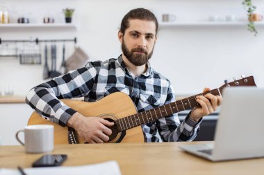 Gülümseyen beyaz adam bilgisayardan online dersler alarak enstrüman çalmayı öğreniyor. Altı telli gitarla poz veren yakışıklı sakallı bir yetişkinin portresi..