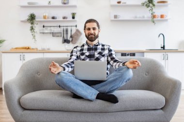 Diz çöküp meditasyon yapan, kablosuz laptopuyla koltukta oturan, günlük kıyafetli, barışçıl Kafkas işadamı. Mudra jestinde parmakları olan sakallı genç adam stresi azaltır ve enerjisini geri kazanır..