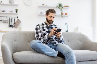 İşveren için kapalı alanda proje yaparken meslektaşına mesaj atan verimli bir serbest çalışan. Evde modern işyerinde kalırken elinde akıllı telefon tutan kareli gömlekli beyaz bir erkek..