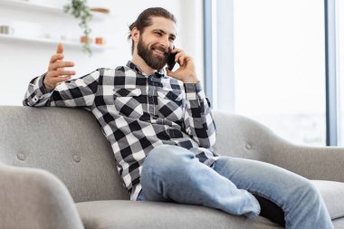 Güneşli bir günde cep telefonuyla sohbet ederken koltukta oturan gülümseyen iş adamının yan görüntüsü. Profesyonel Kafkas yöneticisi evdeki açık mutfak raporunu tartışıyor..