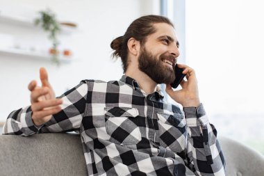 Profesyonel Kafkasyalı yönetici evdeki açık mutfak raporunu tartışıyor. Güneşli bir günde cep telefonuyla sohbet ederken koltukta oturan gülümseyen iş adamının yan görüntüsü.