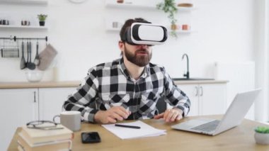 Neşeli sakallı adam VR kulaklık takıyor ve mutfakta çalışırken mutluluktan el kol hareketi yapıyor. Kafkas Teknoloji Yöneticisi yeni modern aygıtlardan memnun.