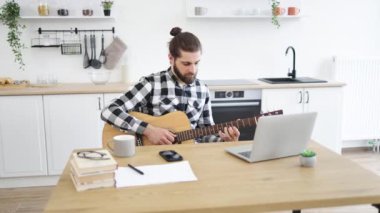 Gülümseyen beyaz adam bilgisayardan online dersler alarak enstrüman çalmayı öğreniyor. Altı telli gitarla poz veren yakışıklı sakallı bir yetişkinin portresi..
