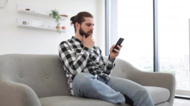 İşveren için kapalı alanda proje yaparken meslektaşına mesaj atan verimli bir serbest çalışan. Evde modern işyerinde kalırken elinde akıllı telefon tutan kareli gömlekli beyaz bir erkek..