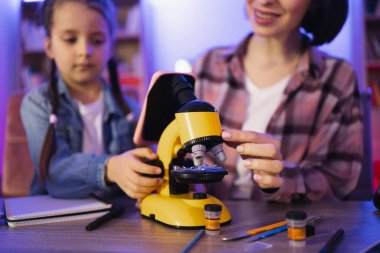 Ebeveynlik ve öğretmenlik kavramı, akşamları evde boş vakit geçirmek. Modern elektronik mikroskopla çalışan günlük giysili okul kızıyla ilgilenen beyaz bir anne..