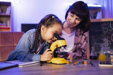 Annesi yanında oturup işlemleri kontrol ederken elektron mikroskobuyla soğan hücrelerine odaklanmış küçük bir kız. Aile kavramı ve akşam vakti birlikte vakit geçirme kavramı..