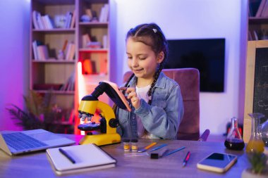 Akşamları evde bilim yaparak günlük kıyafet kursuna giden beyaz bir çocuk. Masada oturan gülümseyen küçük bir kızın portresi akıllı telefon kullanarak elektron mikroskobuna bakıyor..