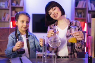 Genç annesiyle oynayan konsantre küçük kız akşamları evde kimya deneyleri yapıyor. Küçük kızını evde eğiten mutlu bir anne, biyolojik testler yapıyor..