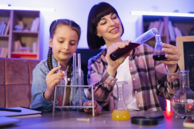 Beyaz bir anne zeki kızıyla kimyasal deneyler ya da testler yaparken şişelerden ve deney tüplerinden sıvıları karıştırıyor. Değer veren bir kadın ve küçük bir kız. Akşam evde bilgiyi geliştiriyorlar..