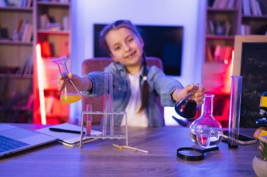 Altı yaşında, günlük giysiler içinde, masada oturmuş kimya ekipmanlarıyla oynayan küçük beyaz bir bilim kadını. Anaokulunda akşam evde öğrenim ve eğitim deneyleri yapan mutlu bir çocuk..