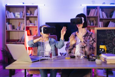 Küçük beyaz kız, ablasını kimyasal test yaparken izliyor ve sanal gerçeklik kulaklığı takıyor. Meraklı okul kızı annesiyle oynuyor. Video gözlüğü kullanarak komik bir deney yapıyor..