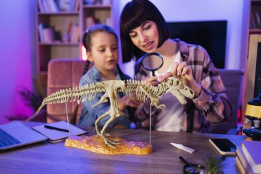 Sıradan giyinen genç bir kadın küçük bir kızla masaya oturur ve büyüteçle dinozor iskeletini inceler. Anne ve kızı evde kemiklerden Tyrannosaurus modeli yapıyorlar..
