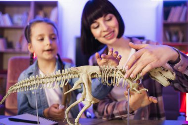 Masada birlikte oturan iki dişi akşam vakti evde kemiklerden Tyrannosaurus 'un modelini yapıyorlar. Kafkas anne ve kızı fosil hayvanlar üzerinde çalışıyorlar dinozor iskeletini inceliyorlar.