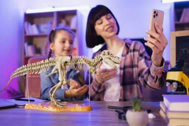 Genç kadın ve küçük tatlı kız bilimsel araştırmalarını videoya çekiyorlar. Mutlu anne dinozor iskeletini inceliyor ve akıllı tatlı kız doğal blog için içerik kaydediyor..