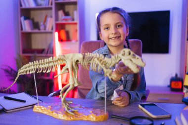 Kot gömlekli küçük kız akşamları evde doğa bilimi öğreniyor kemiklerden tiranozor modeli yapıyor. Çocukluğu ve okulu, ödevi kavramsallaştır.
