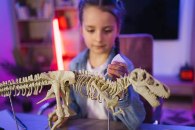 Masada oturmuş dinozorun iskeletini inceleyen günlük giysiler içinde altı yaşında beyaz bir bilim kadını. Mutlu anaokulu çocuğu kemikleri yapıştırıyor akşam evde Tyrannosaurus 'un modelini yapıyor..