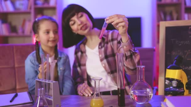 ナニー ベビーシッター 教師と自宅での科学実験 学校の宿題のための実験室テスト 自宅のリビングルームで夕方に化学検査をする娘の子供を持つ親の母親 — ストック動画