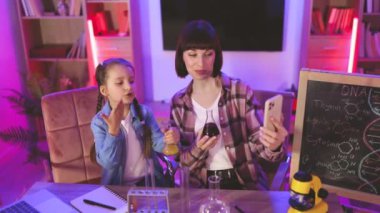 Mutlu anne bilimsel blog için içerik kaydeden zeki bir kızla kimyasal deneyler veya testler yapıyor. Genç kadın ve küçük tatlı kız bilimsel araştırmalarını videoya çekiyorlar..