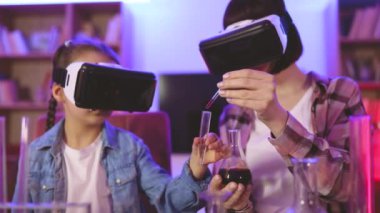 Küçük bir kıza evde VR gözlüğü kullanarak kimyasal deneyler yapmayı öğreten şefkatli bir anne. Akşam vakti sanal gerçeklikte yer alan mutlu iki nesil ailesi, çocuk gelişimi kavramı.