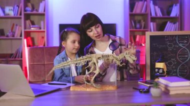Kafkas anne ve kızı masada oturup büyüteçle dinozor iskeletini inceliyor. Tarih öncesi araştırmalara katılan iki kadın gece evde kemikleri olan tiranozorların modelini yapıyorlar.