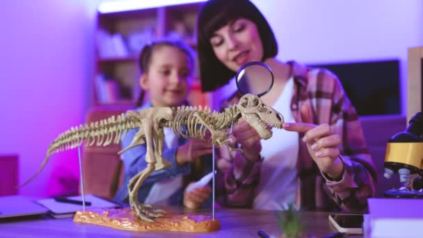 快乐的小女儿和她的母亲坐在一起吃饭 晚上用放大镜研究化石动物 两名身穿休闲装的白人妇女进行史前研究 — 图库视频影像