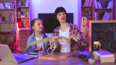 Mutlu anne, dinozor iskeletini inceliyor ve güzel kızı da doğal blog için içerik kaydediyor. Genç kadın ve küçük tatlı kız bilimsel araştırmalarını videoya çekiyorlar..